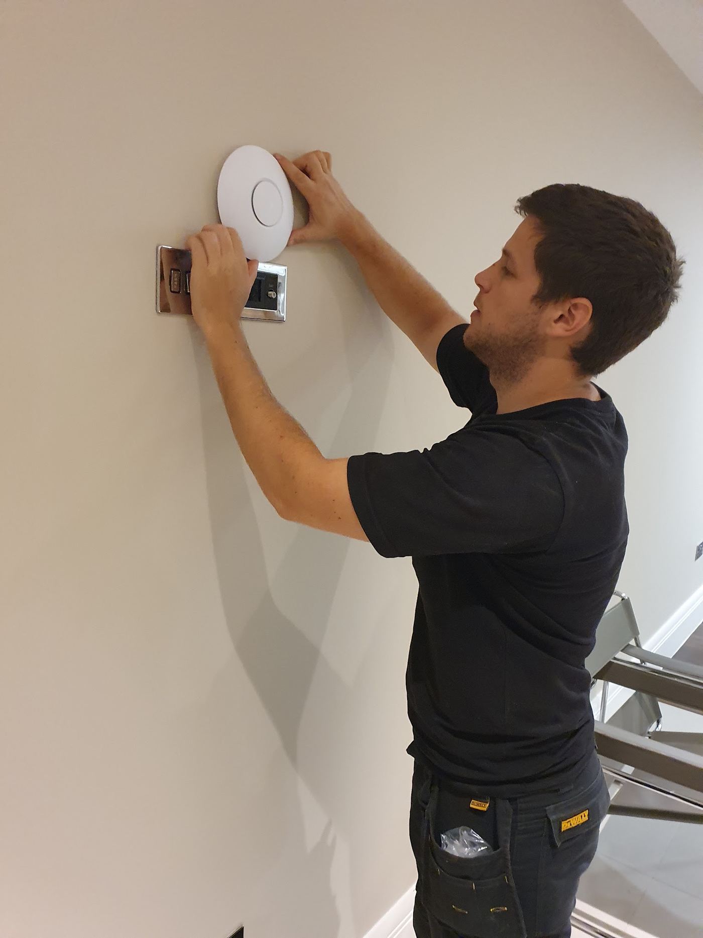 AV Infusion engineer fitting a wall-mounted WiFi access point above a network socket