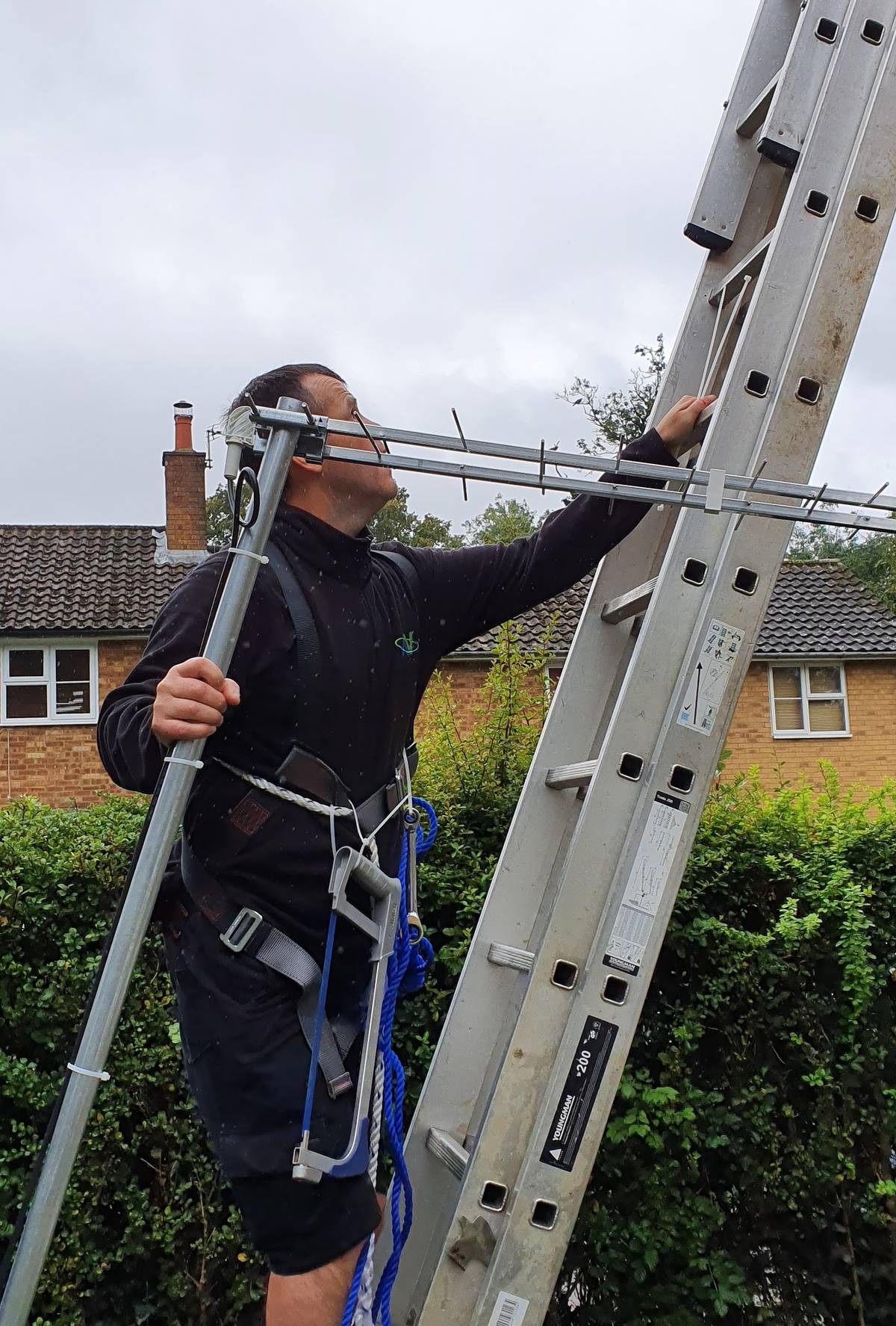 AV Infusion engineer fitting a TV aerial bracket at height on a ladder with full safety harness